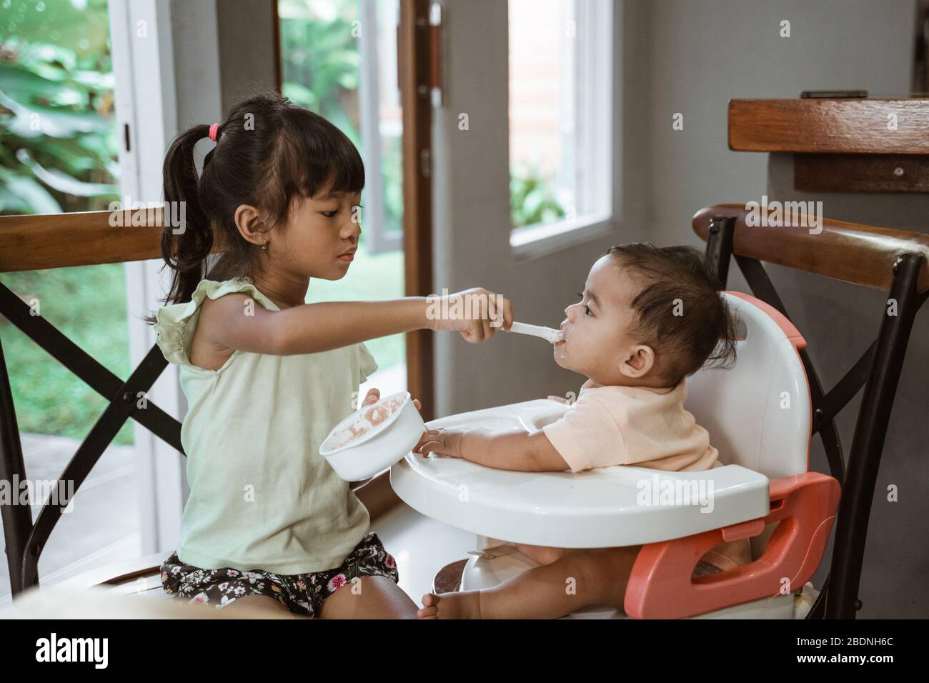sibling feeding her little baby sister at home Stock Photo Alamy