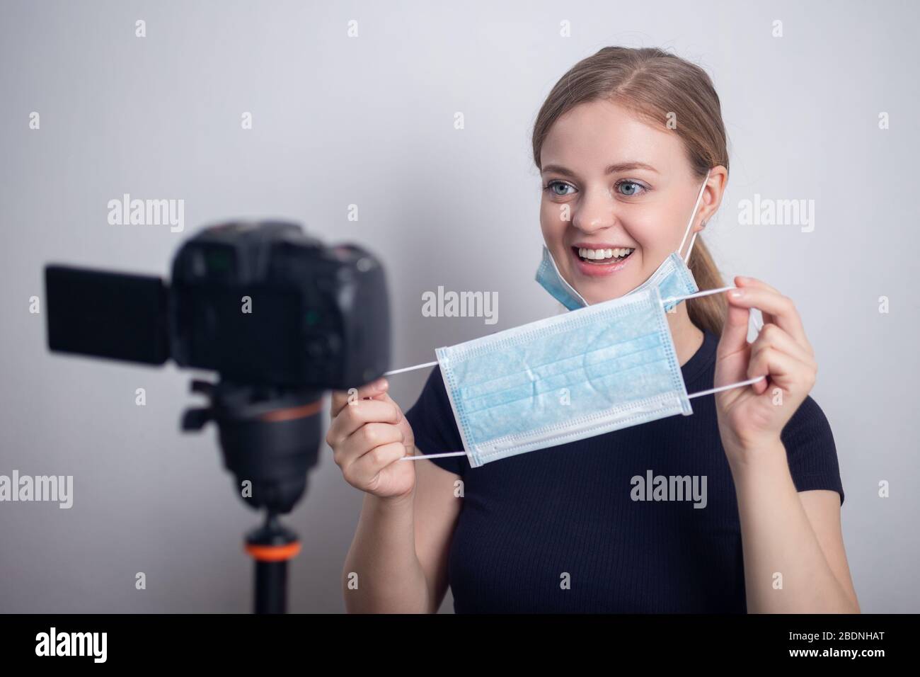 Smiling young caucasian girl woman wearing mask, making a video blog (vlog) with camera at home Stock Photo