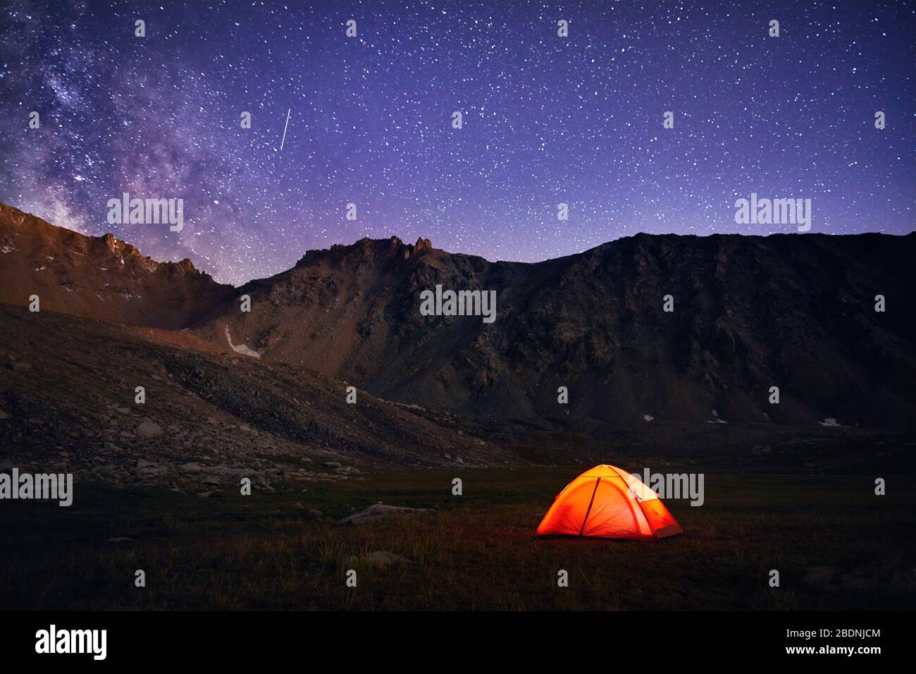 Orange tent glows under night sky full of stars and Milky way in the ...