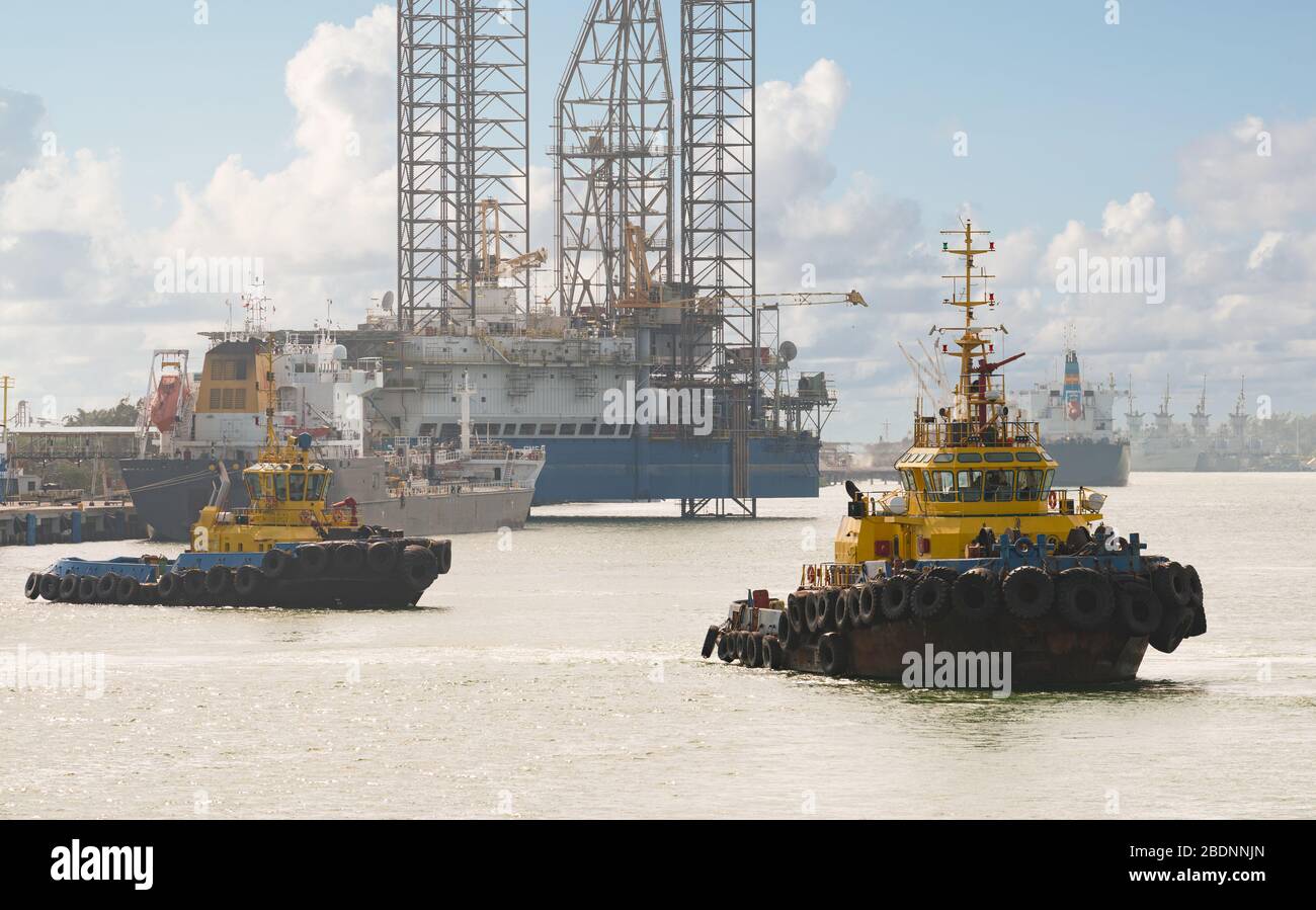 Tug boats awaiting big cargo ship in harbour for tug assistance, maneuvering, mooring operations. Tugboat and tow service concepts. Stock Photo