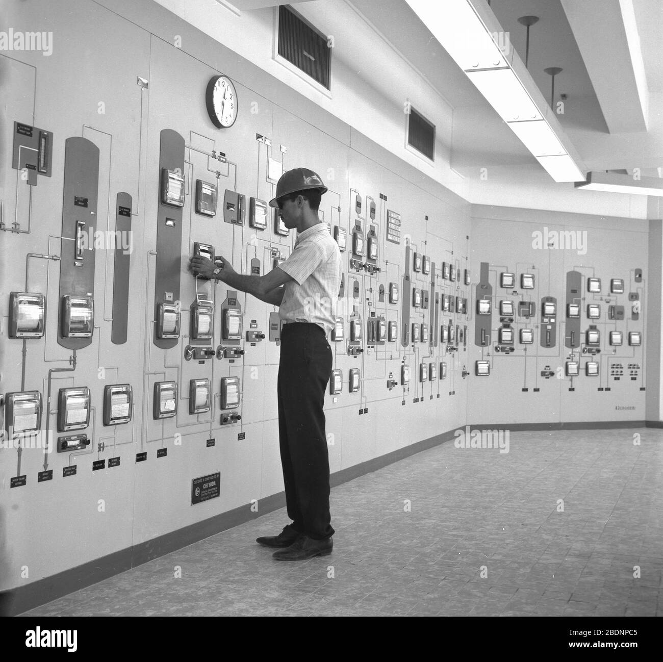 1960s, historical, a male worker wearing a hard-hat standing inside a large control room full of wall-mounted instruments and indicators, possibly at an oil refinery or oil related processing plant, Saudi Arabia. Stock Photo
