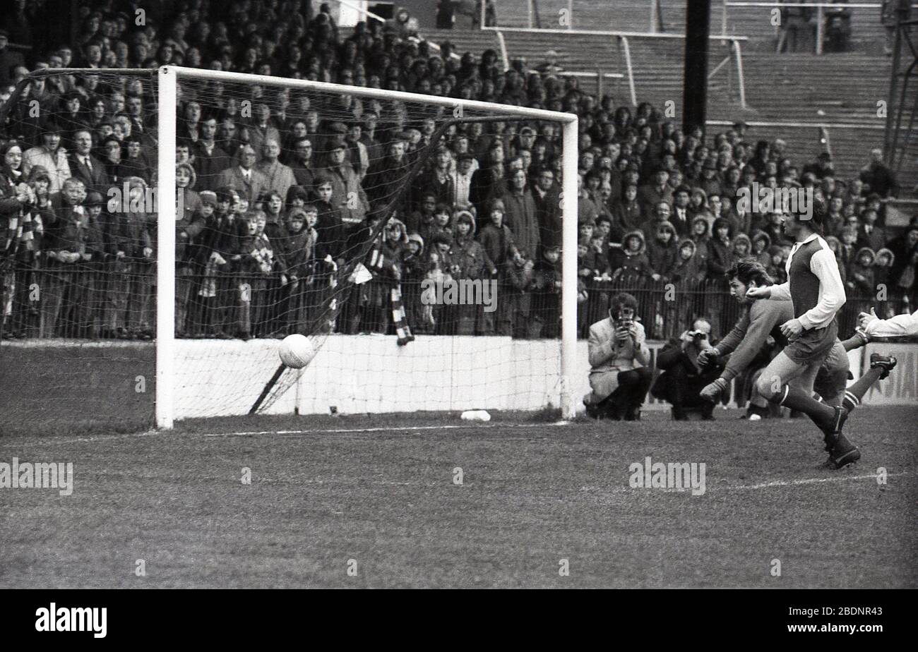 1973, historical, a goal being scored at the Valley, the home of Charlton Football Club, the reason the he crowd standing behind the goal are not jumping up is that it is the oppostion scoring! Notice on the right of the picture, how steep the terraces are and the 'safety' metal barriers. Other things to notice, the photographers are right by the goalposts, and not wearing 'bibs' and the crowd are not wearing replica football shirts, just scarfs. Stock Photo
