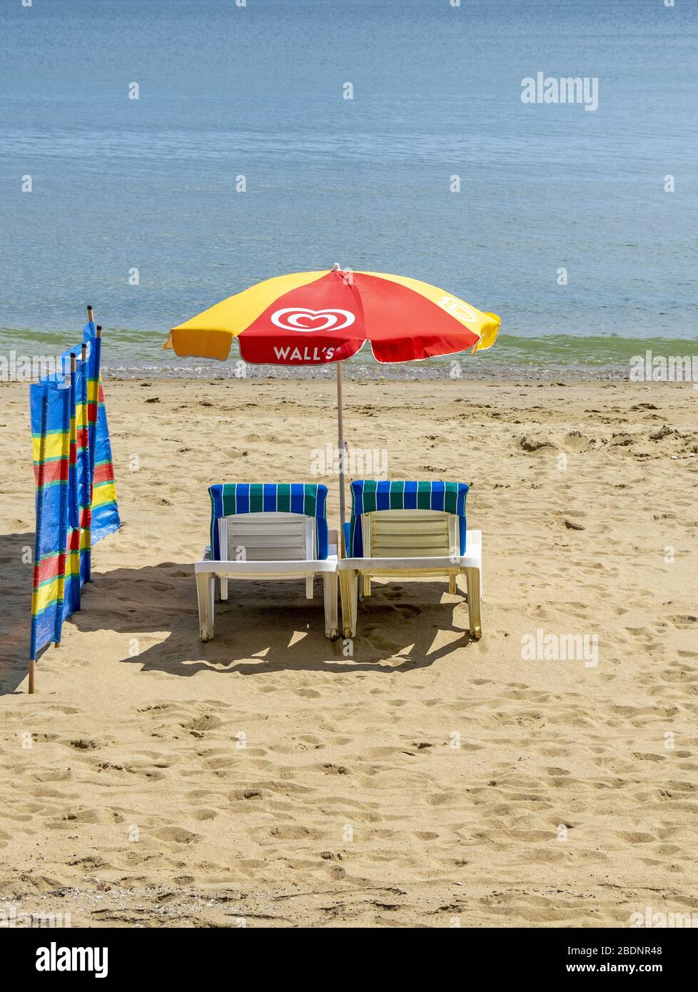 Empty sunloungers, a wind breaker and sun umbrella setup on beach Stock Photo