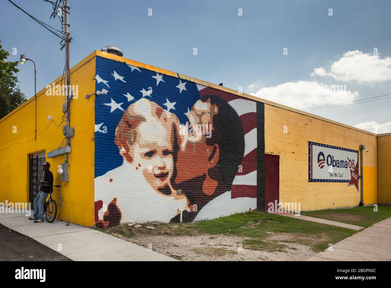 Obama’s Mural of electoral propaganda on a yellow wall close to a black race man leaning on a bicycle, West Alabama St, Midtown, Houston Texas Stock Photo