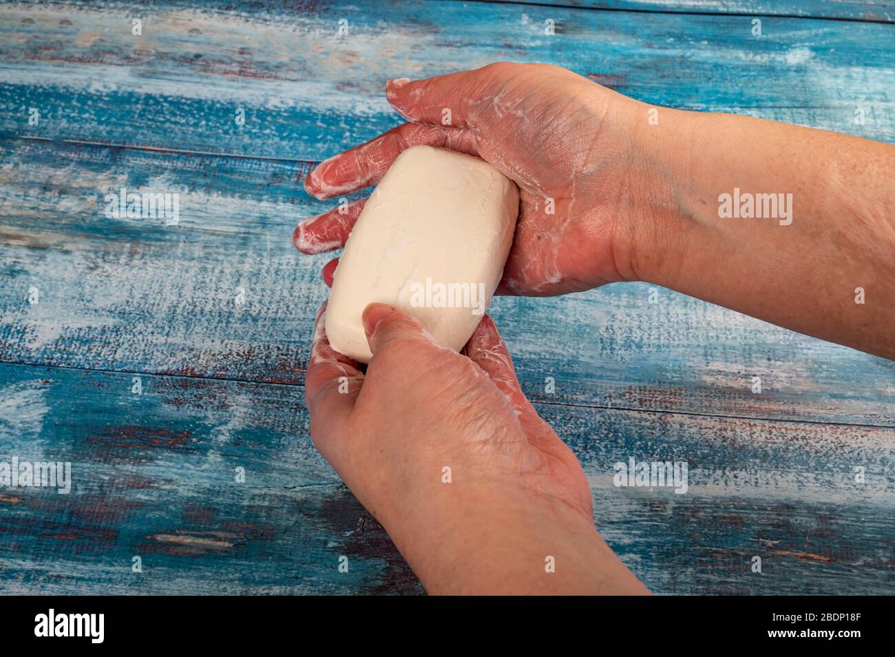 Someone is soaping their hands with a piece of toilet soap on a wooden ...