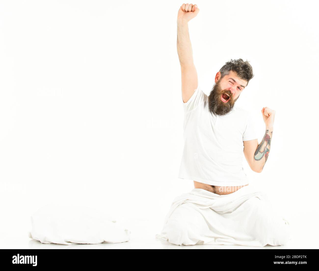 Man stretching and yawning, waking up, sit on floor. Tattooed man with beard stretch his arms while sit near pillow in morning, top, view Stock Photo