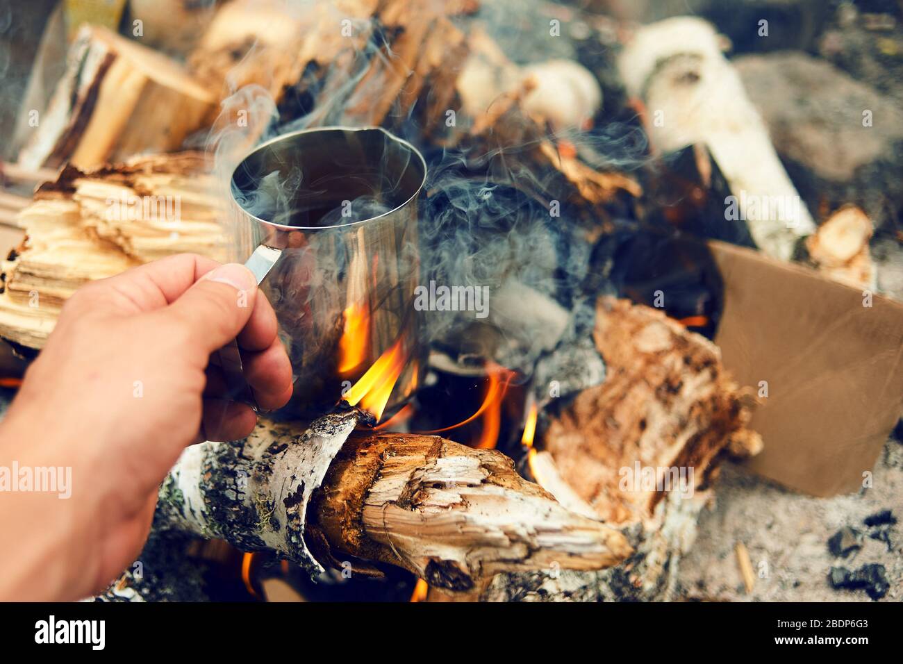 https://c8.alamy.com/comp/2BDP6G3/man-traveler-hands-holding-cup-of-tea-near-the-fire-outdoors-hiker-drinking-tea-from-mug-at-camp-coffee-cooked-over-a-campfire-on-the-nature-2BDP6G3.jpg