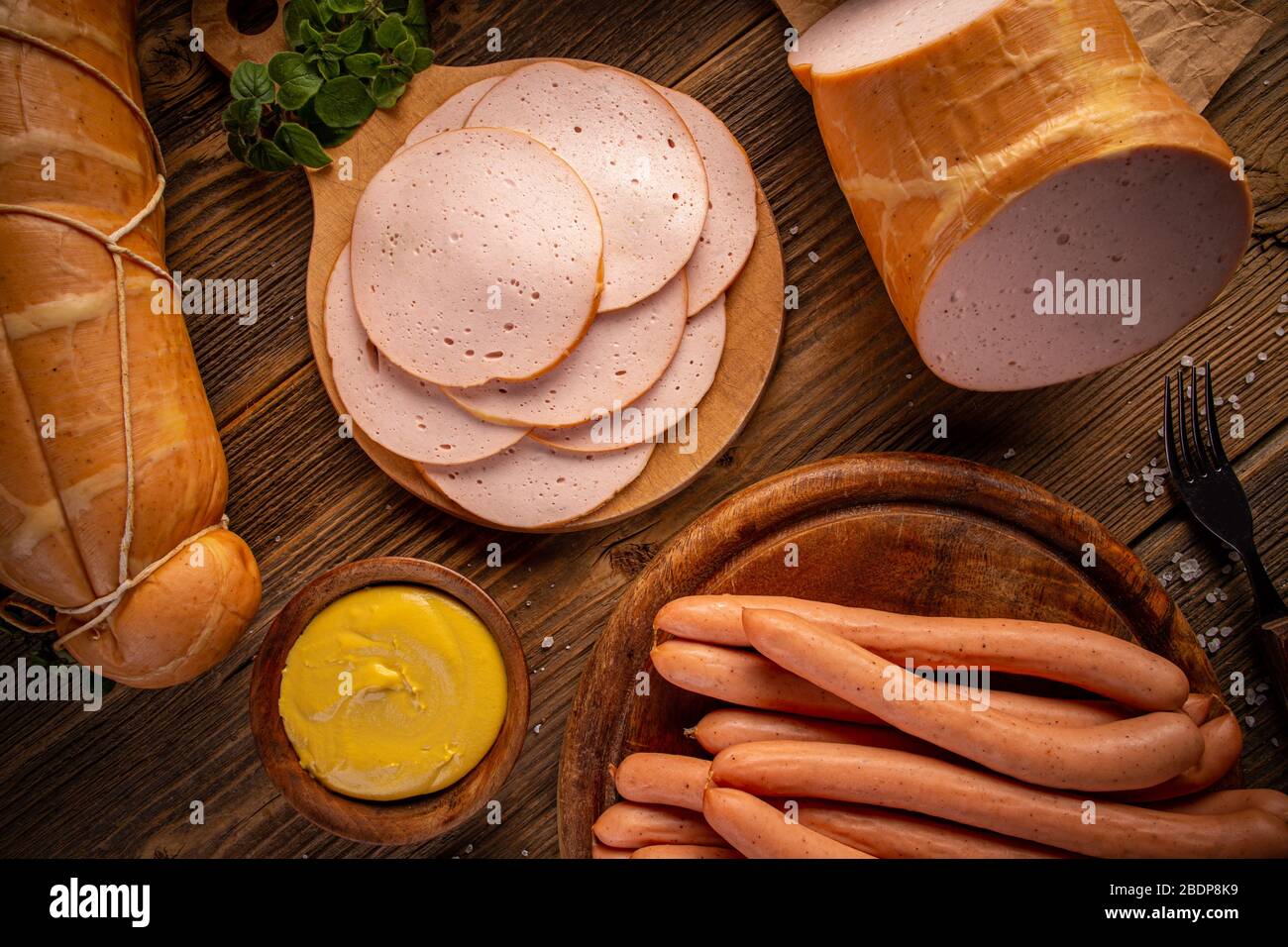 Composition of deli meats and Wiener sausages served with mustard on wooden cutting board, flat lay Stock Photo