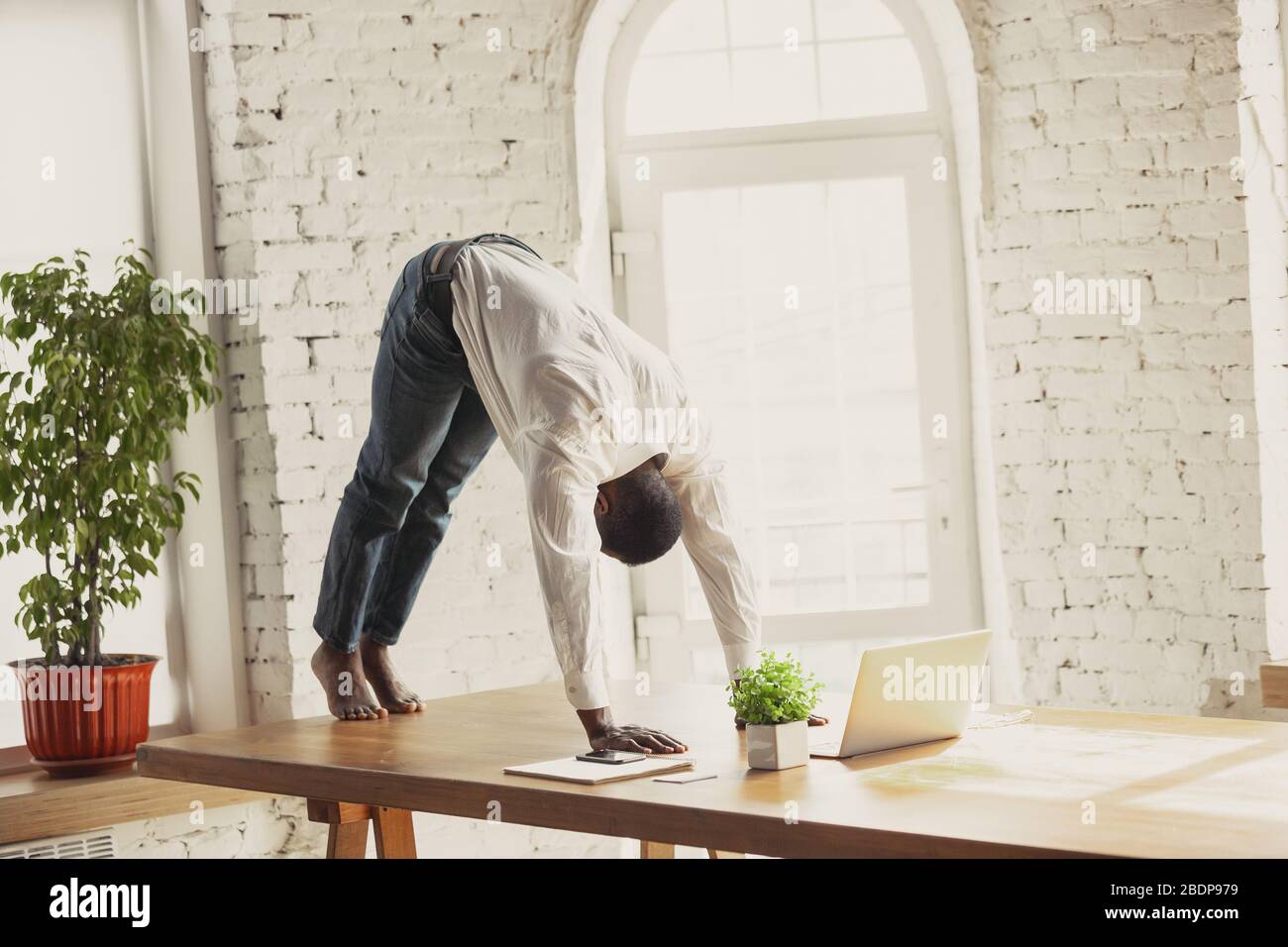 https://c8.alamy.com/comp/2BDP979/young-african-american-man-doing-yoga-at-home-while-being-quarantine-and-freelance-online-working-remote-isolated-or-alone-at-office-concept-of-healthy-lifestyle-wellness-activity-movement-2BDP979.jpg