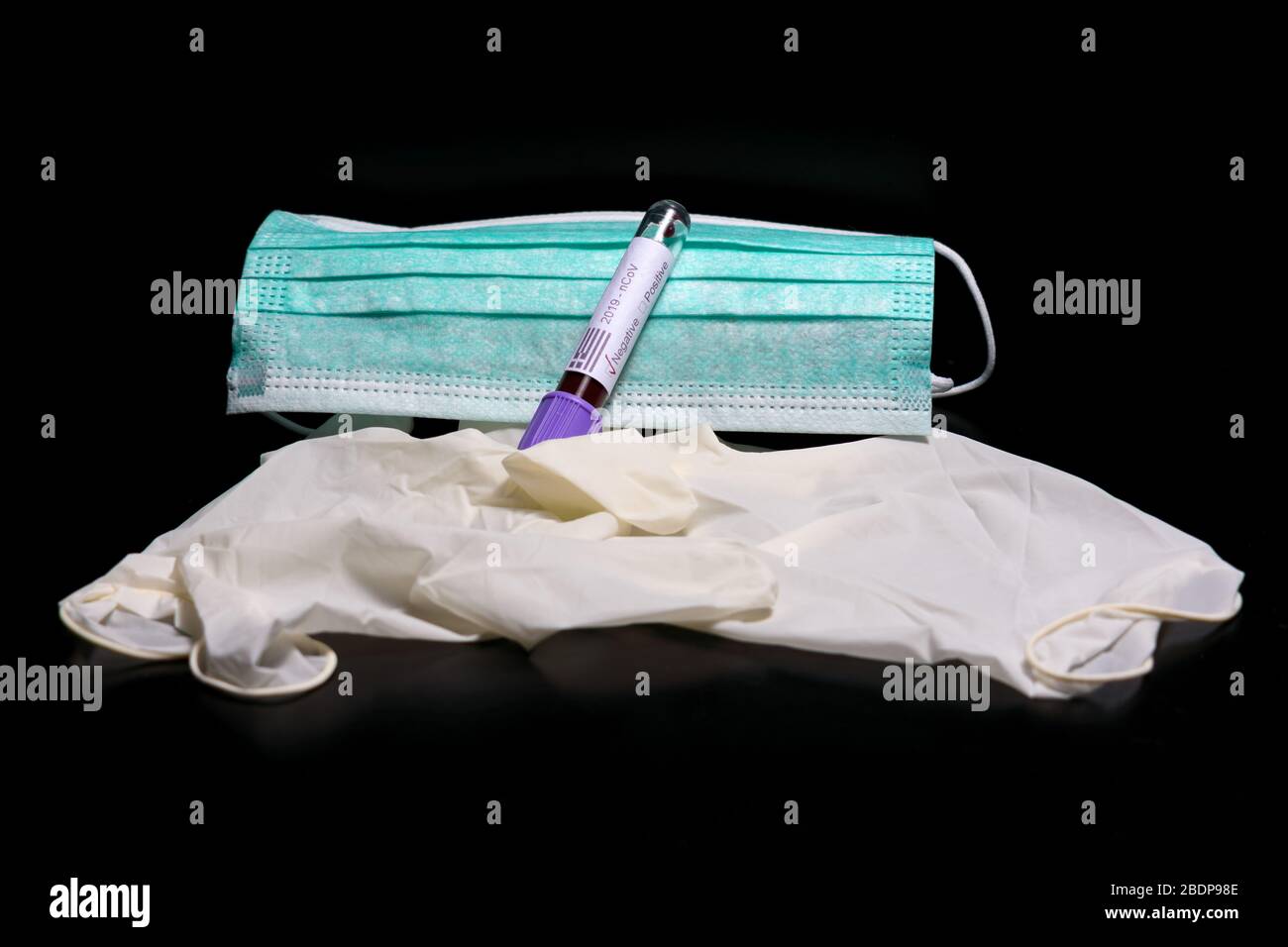 A  blood vial in front of a medical mask and disposable gloves. The label on the vial states 2019 n Cov, the words positive negative. Stock Photo
