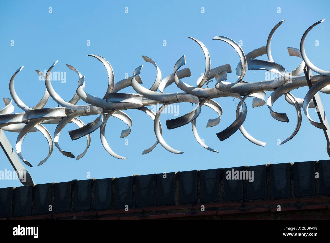 Tall and high brick wall with modern rotating security barrier with curved barbed / razor vane spiked edges on the top of it, for security purposes. (116) Stock Photo