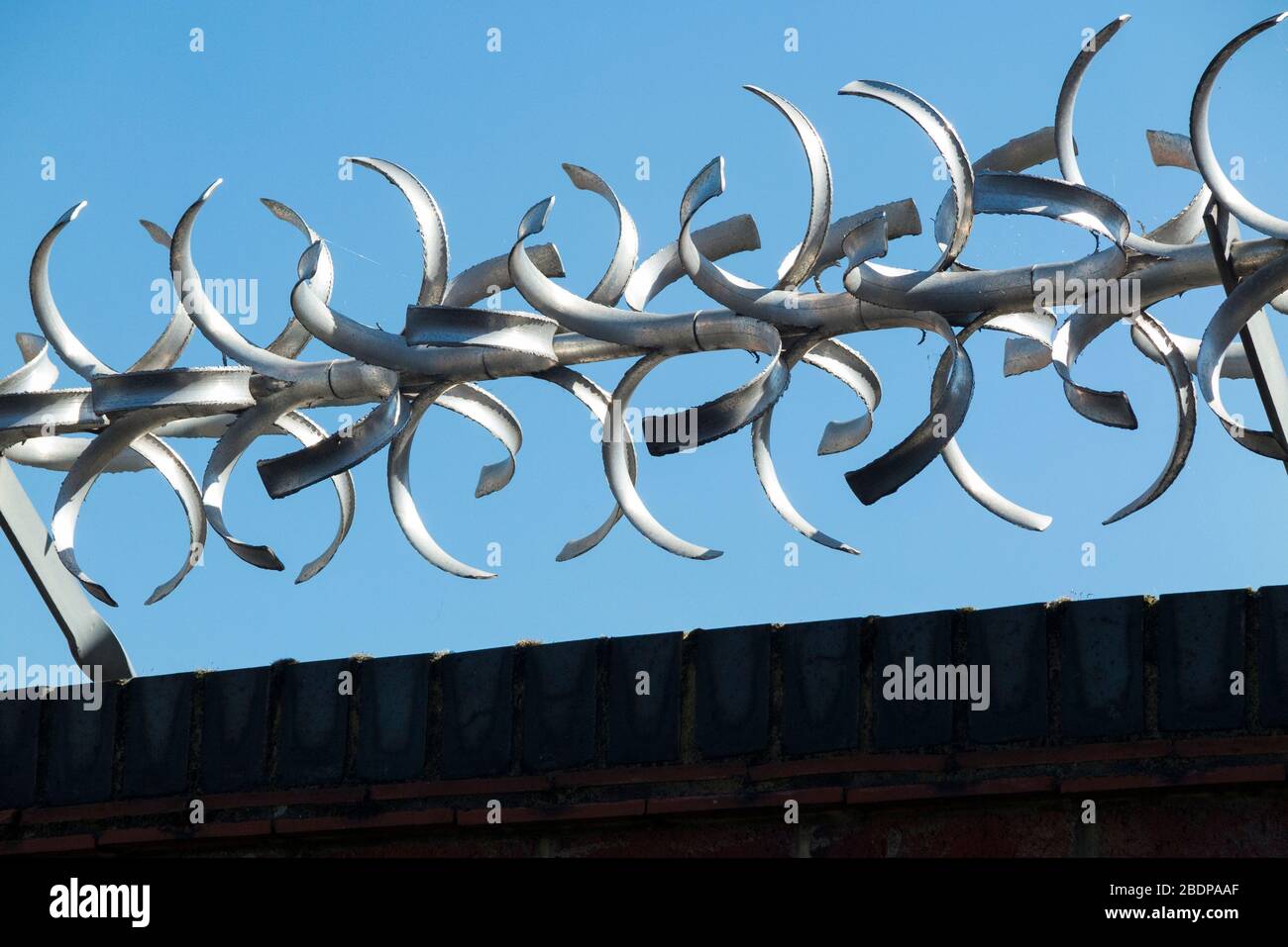 Tall and high brick wall with modern rotating security barrier with curved barbed / razor vane spiked edges on the top of it, for security purposes. (116) Stock Photo