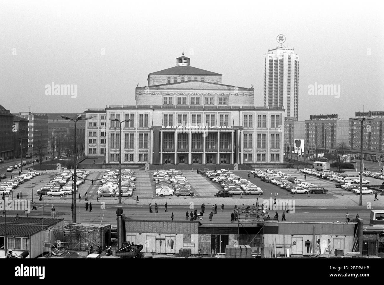 15 April 1980, Saxony, Leipzig: In front of the construction site 'Neues Gewandhaus Leipzig' the appearance of the Karl-Marx-Platz in April 1980 with its old and newly constructed buildings is visible. The picture shows the opera house with the banner 'Long live May 1 - Forward to X. Party Congress of the SED!' and the Wintergartenhochhaus with the double M as well as the Ringbauung. Exact date of recording not known. Photo: Volkmar Heinz/dpa-Zentralbild/ZB Stock Photo