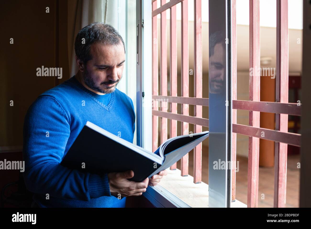 man reading a book by the window dunring quarantine Stock Photo