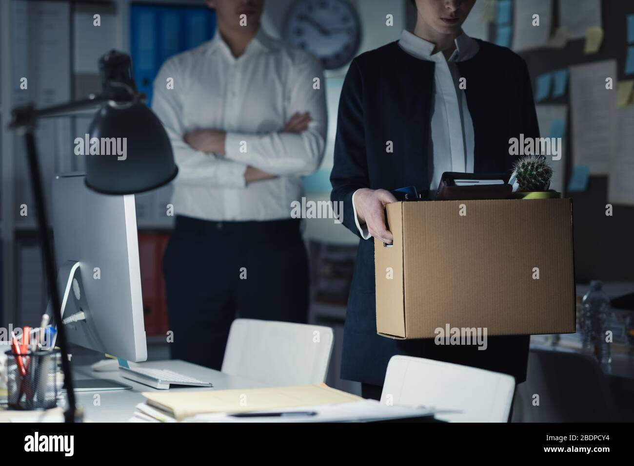 Boss firing a young employee in the office, she is packing her belongings and holding a cardboard box Stock Photo