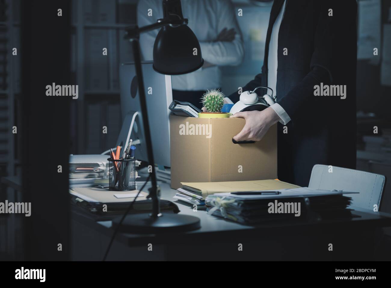 Boss firing a young employee in the office, she is packing her belongings and holding a cardboard box Stock Photo