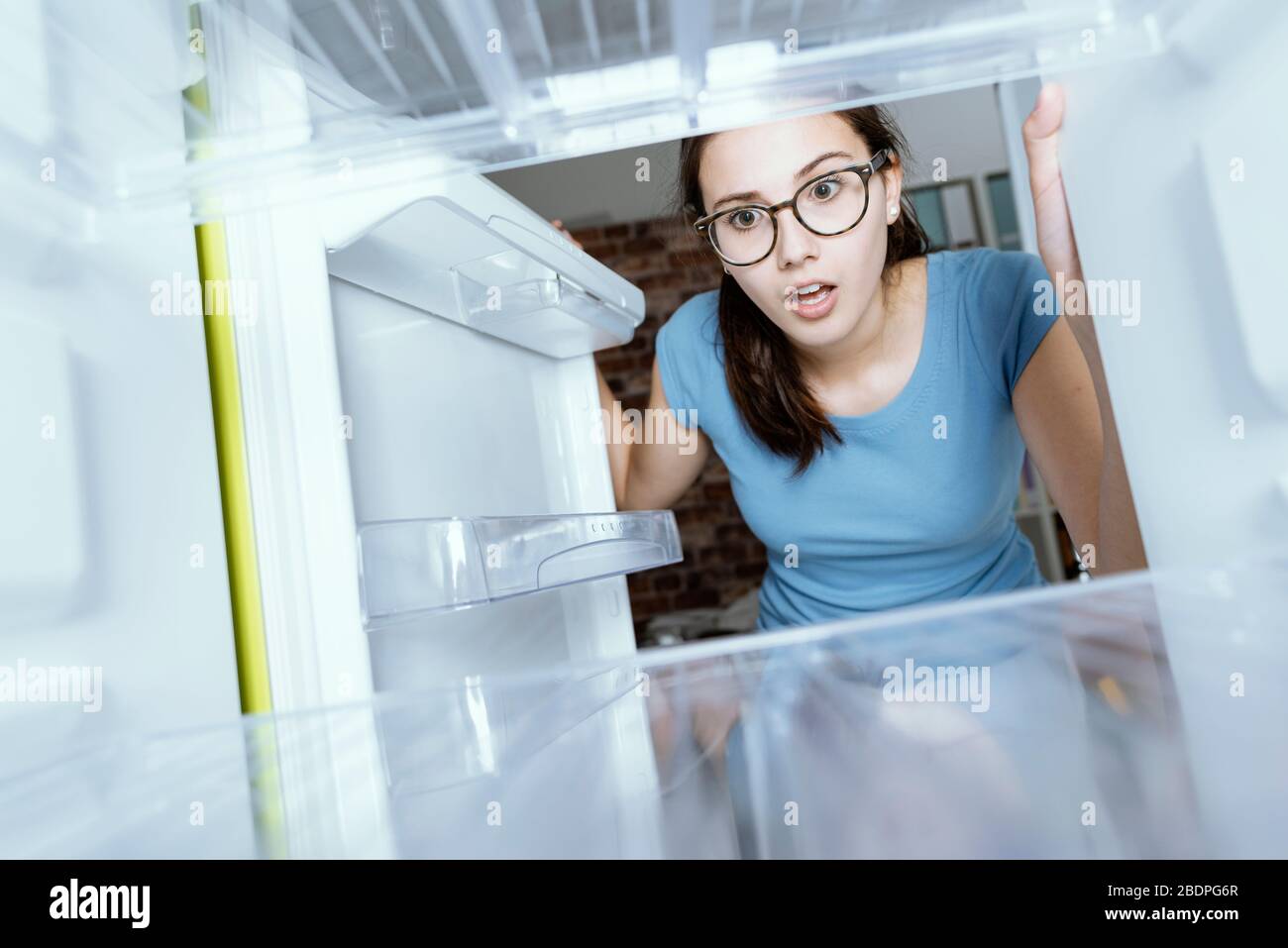 Young hungry desperate woman looking into her empty fridge, she is panicking Stock Photo