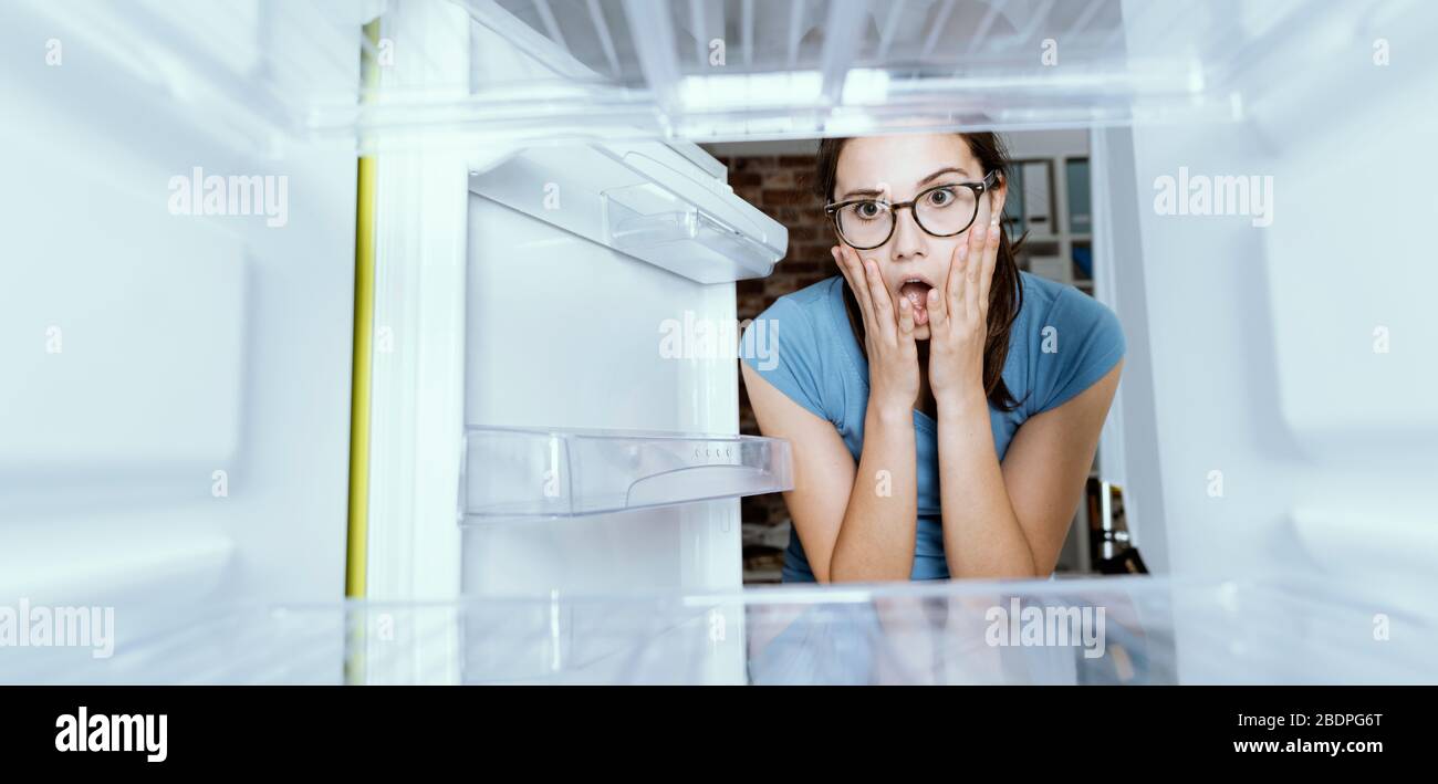 Young hungry desperate woman looking into her empty fridge, she is panicking Stock Photo