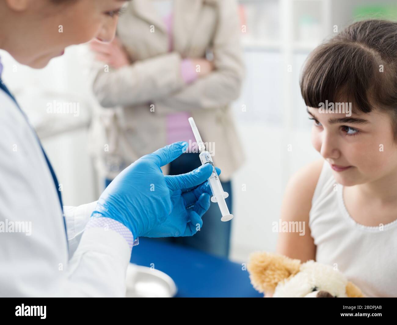 Friendly female doctor showing the syringe to a girl before giving the injection, the girl is relaxed and smiling Stock Photo