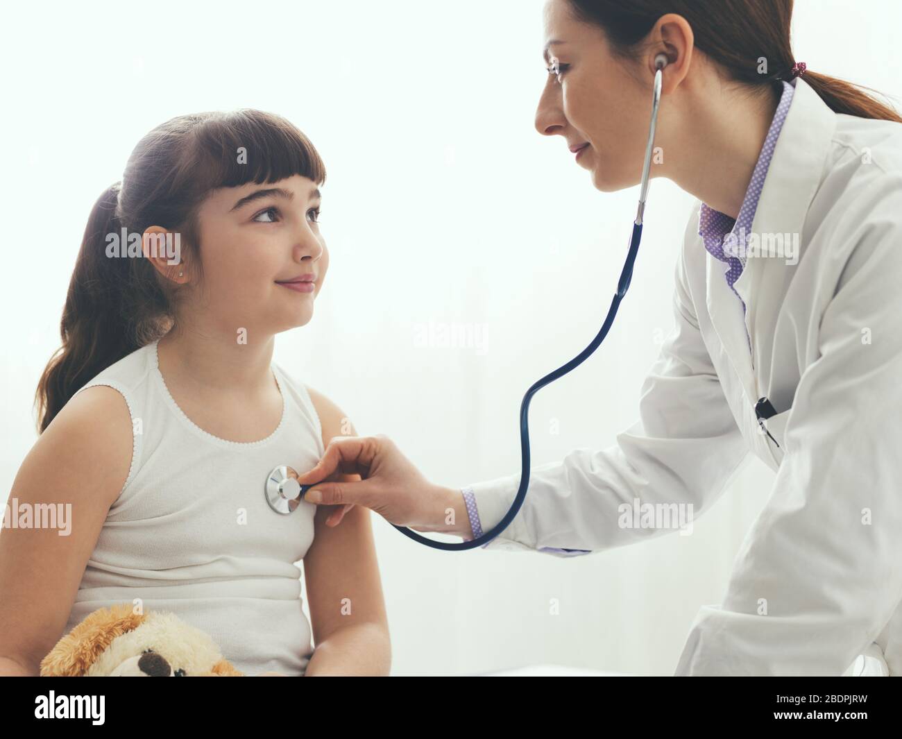 Expert female doctor examining a young girl with a stethoscope, kids and healthcare concept Stock Photo