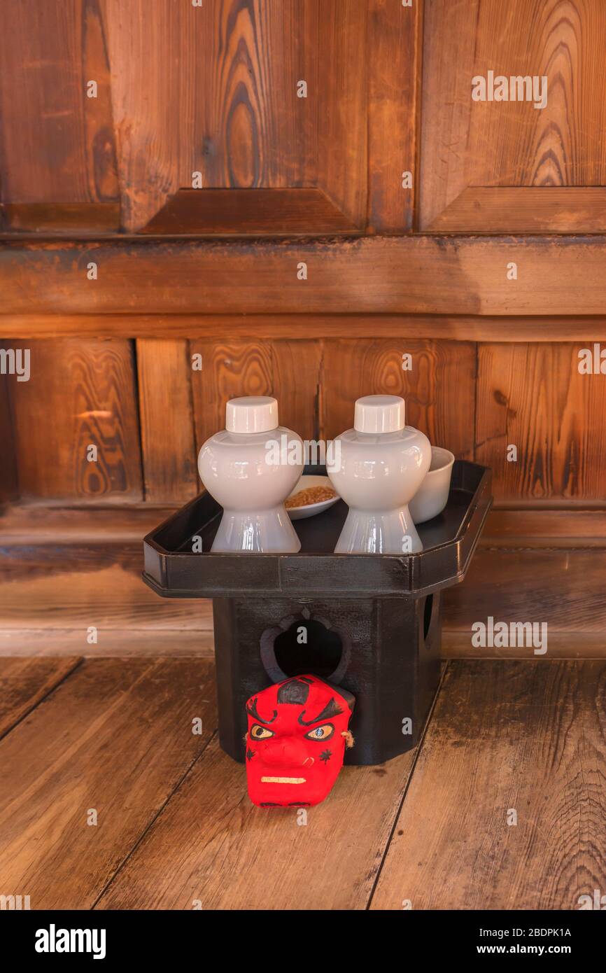 Small red mask of Tengu god of the mountains in front of a black tray sanpou made of cypress wood topped with shinto offerings composed of sake omiki Stock Photo