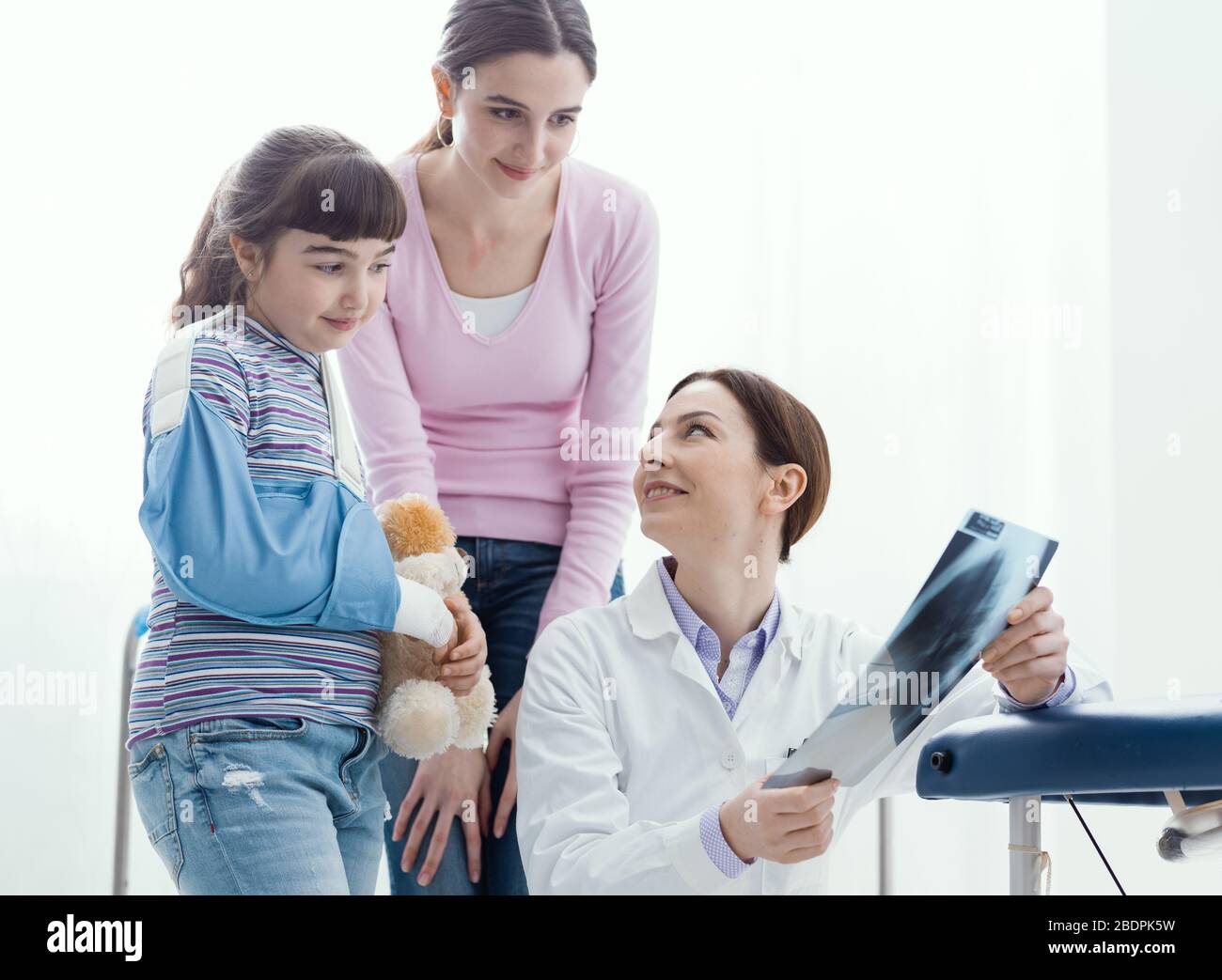 Friendly doctor showing an x-ray image of a broken bone to a young patient, the girl is wearing an arm brace Stock Photo
