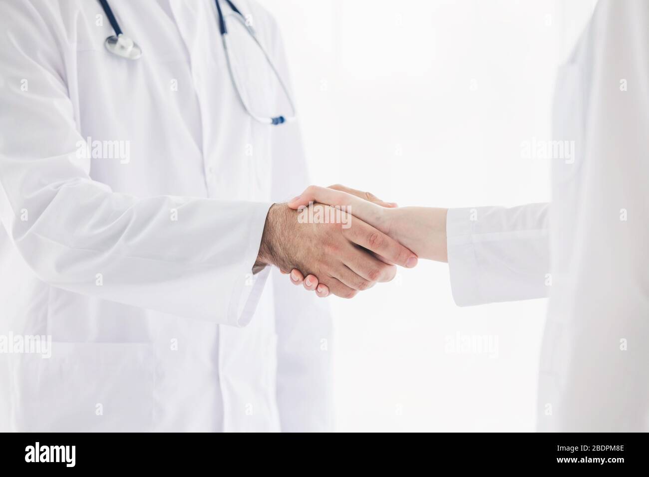Doctors in lab coats greeting each other with handshake Stock Photo