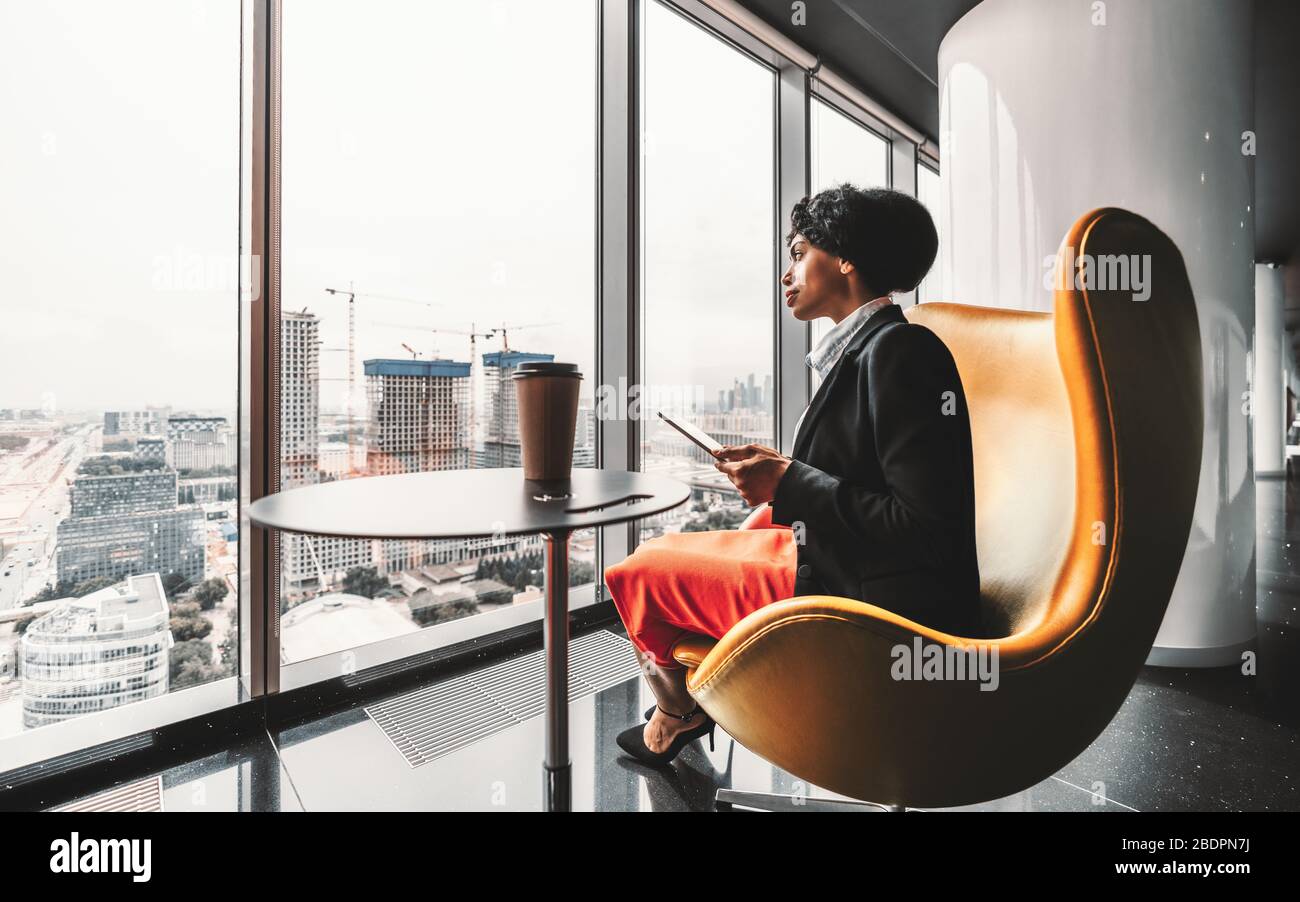 A ravishing African-American businesswoman on a yellow armchair is using her tablet PC; biracial woman entrepreneur using a digital tablet Stock Photo