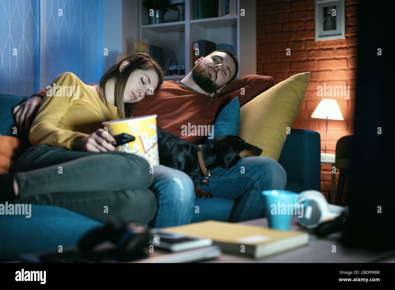 Young sleepy couple sitting on the couch and falling asleep while watching a movie Stock Photo