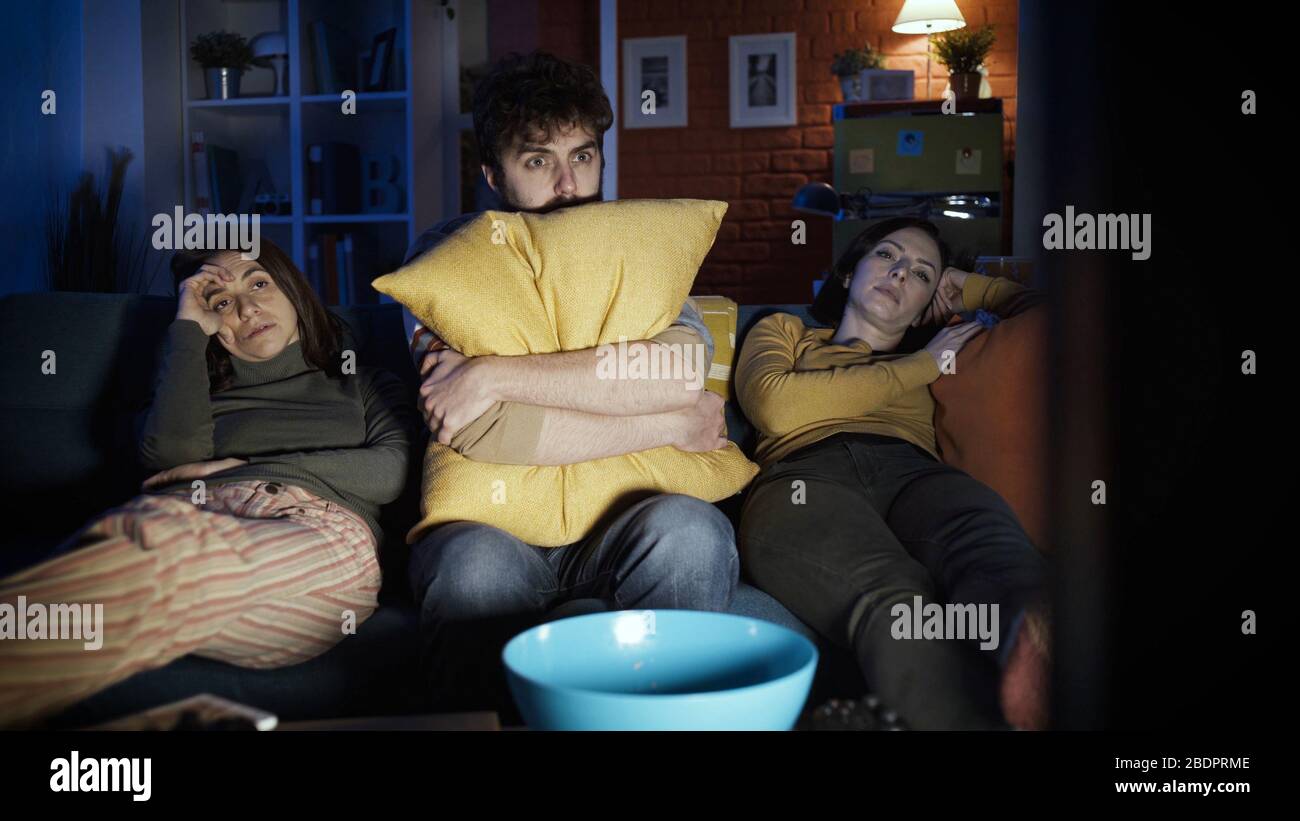 Friends sitting on the sofa at home and watching scary horror movie