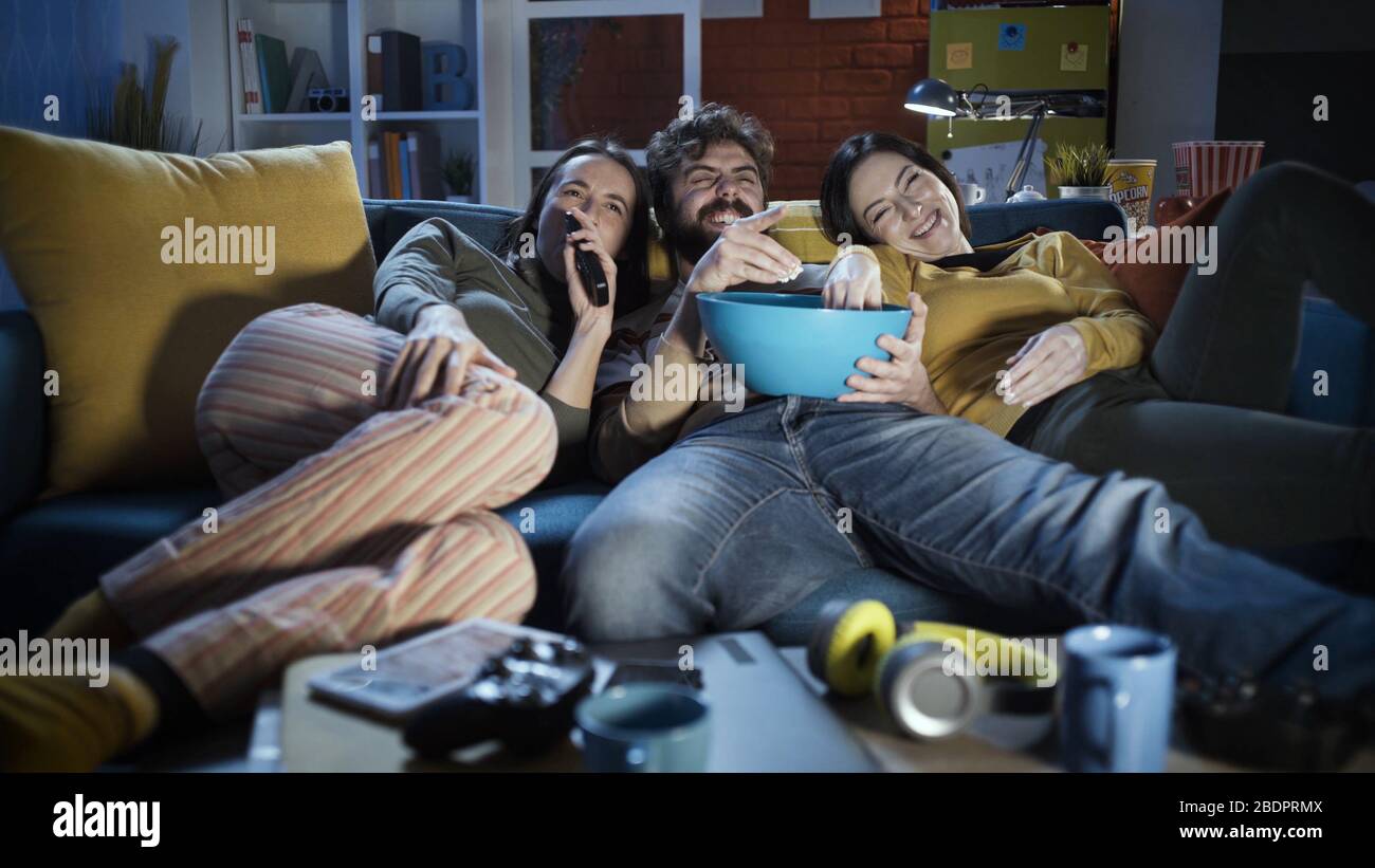 Friends sitting on the sofa at home, they are watching movies and eating popcorn together Stock Photo