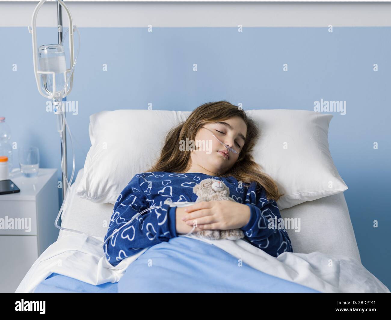 Sick child lying in a hospital bed and holding her teddy bear, kids and healthcare concept Stock Photo