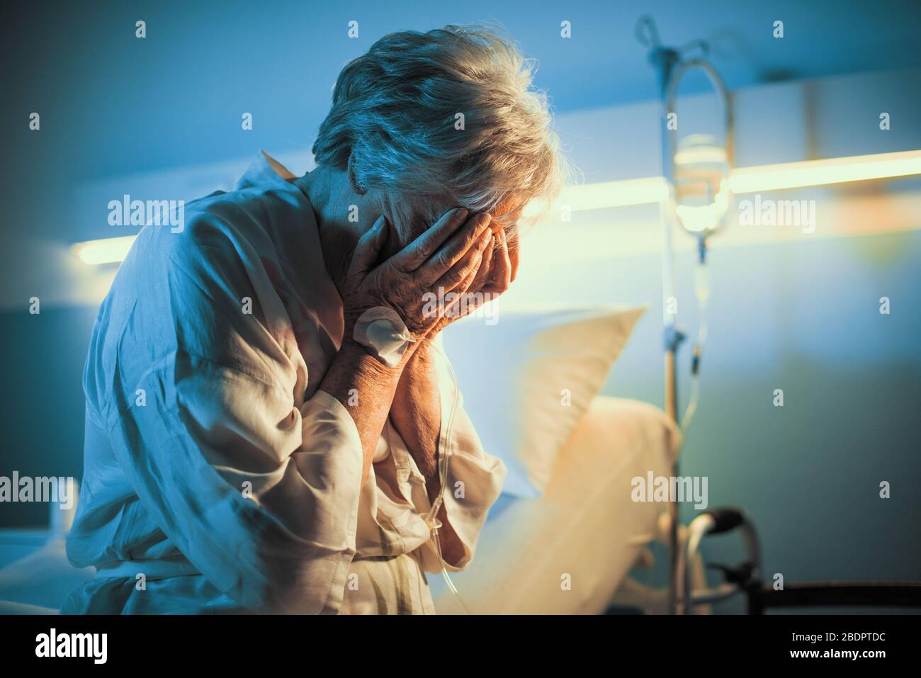 Lonely senior patient sitting on the hospital bed and crying with head in hands Stock Photo