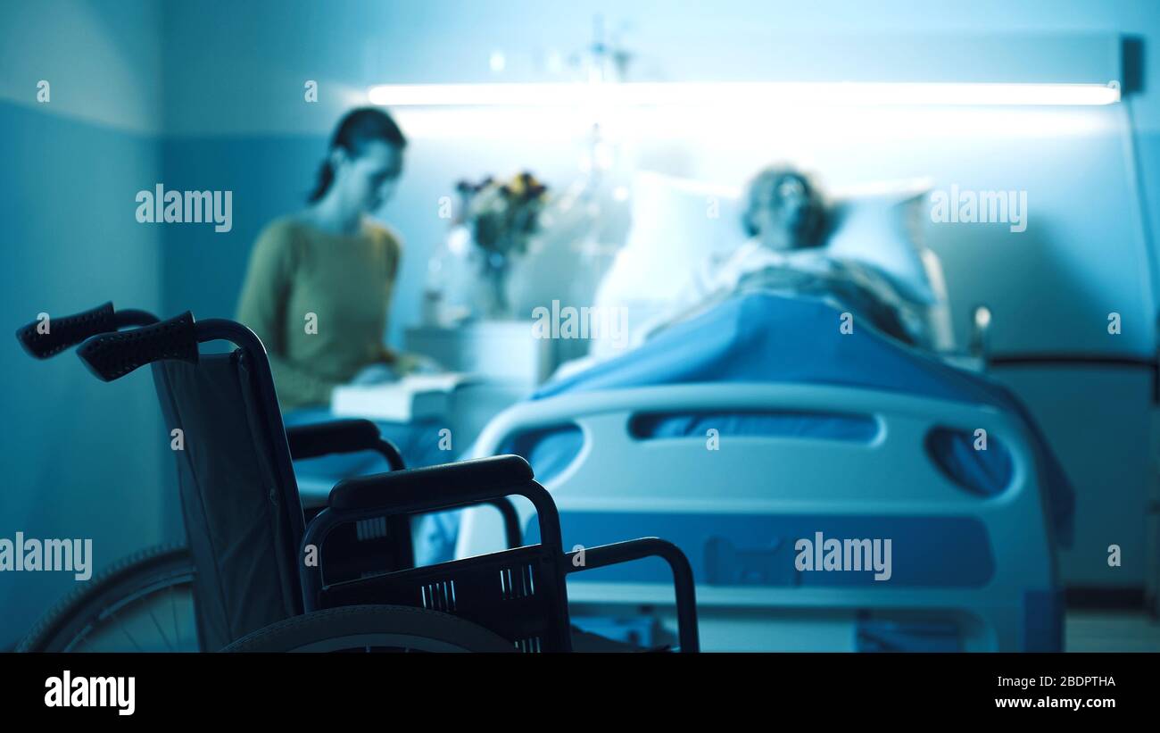 Woman assisting a senior patient at the hospital, wheelchair in the foreground Stock Photo