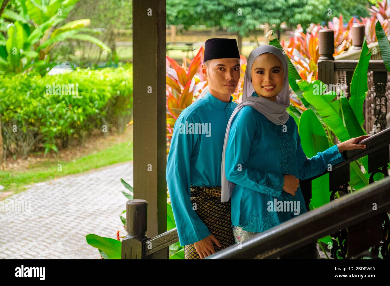 A portrait of young couple of malay muslim in traditional costume during Aidilfitri celebration by traditional wooden house. Raya and Muslim fashion a Stock Photo