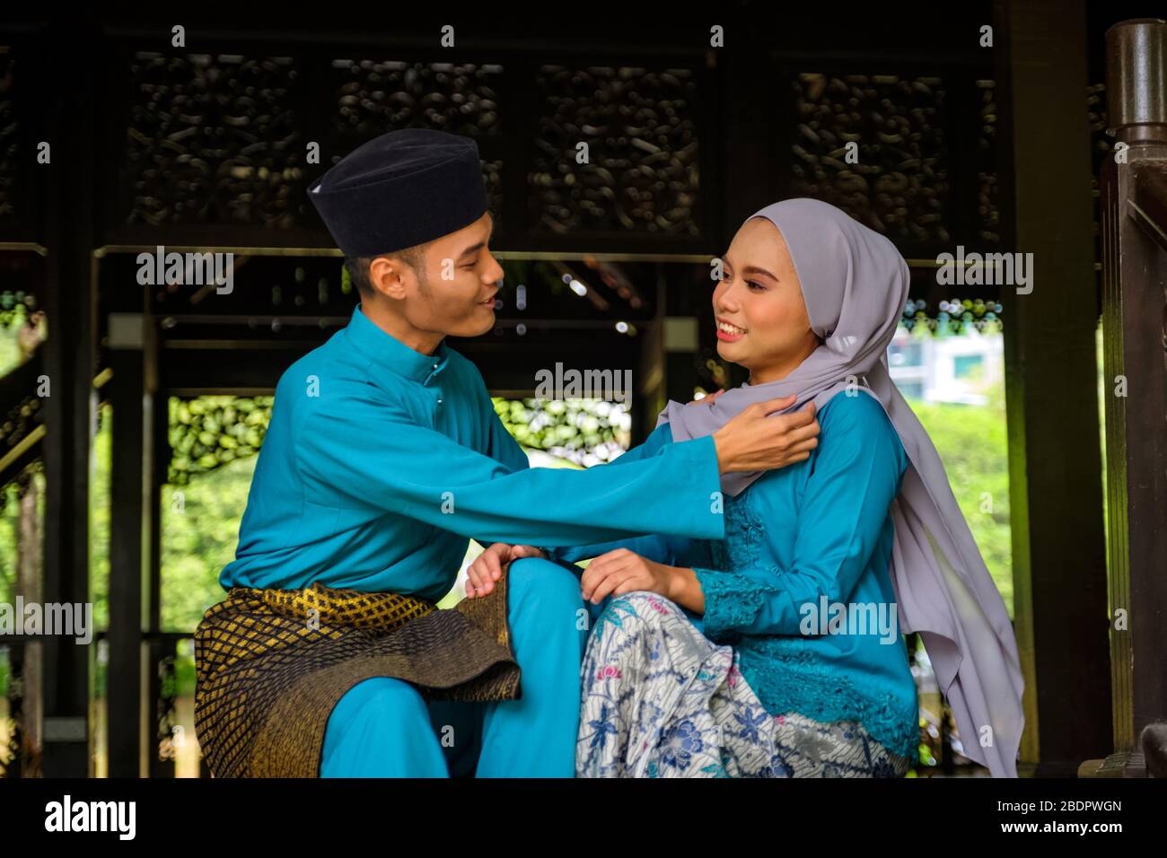 A portrait of young couple of malay muslim in traditional costume showing romantic gesture during Aidilfitri celebration. Man adjusting his girlfriend Stock Photo
