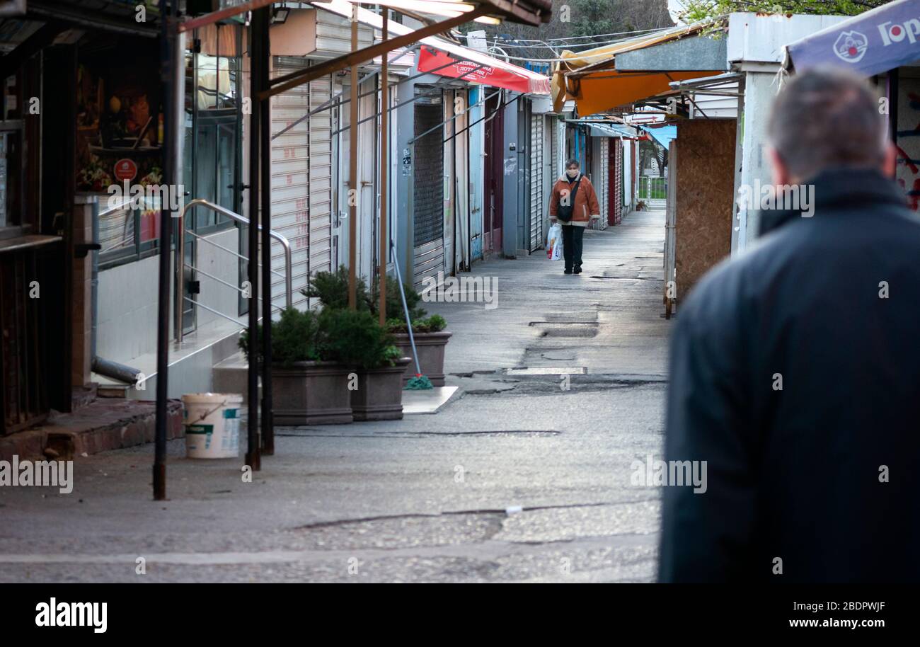 Woman wearing protective face mask is walking in empty market lane with abandoned and deserted shops and small businesses closed down due to economic and industrial decline in the area during the Coronavirus Pandemic of Covid-19 in Sofia Bulgaria Eastern Europe as of 2020 Stock Photo