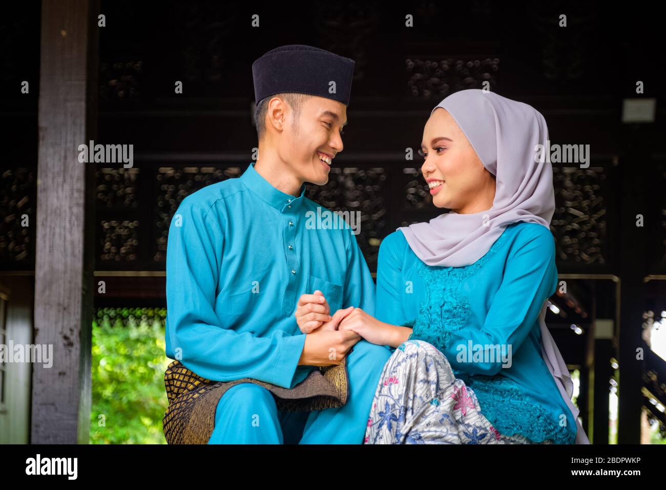 A portrait of young couple of malay muslim looking each other in traditional costume during Aidilfitri celebration at the traditional wooden house. Ra Stock Photo