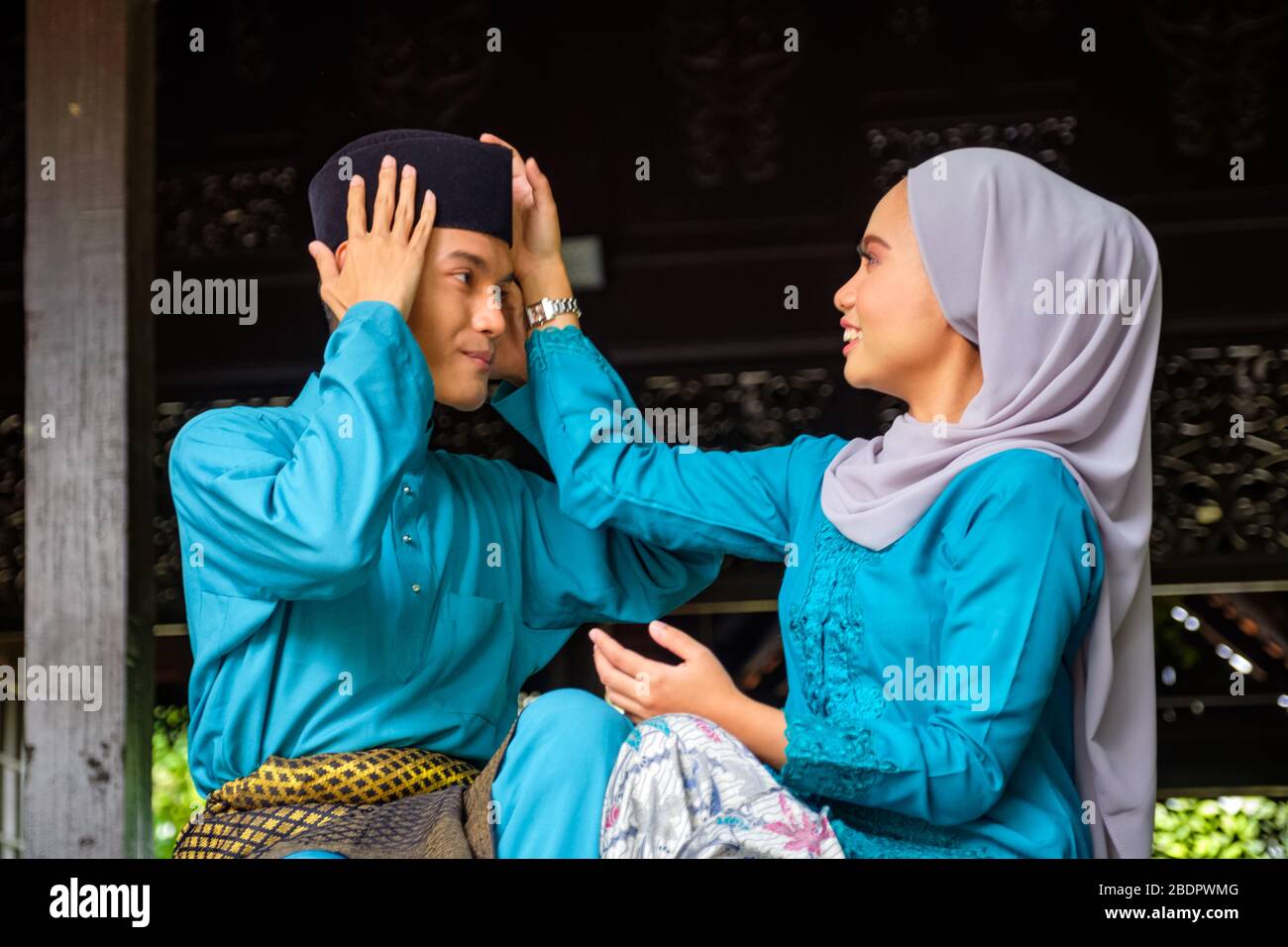 A portrait of young couple of malay muslim in traditional costume showing romantic gesture during Aidilfitri celebration. Girl adjusting his boyfriend Stock Photo
