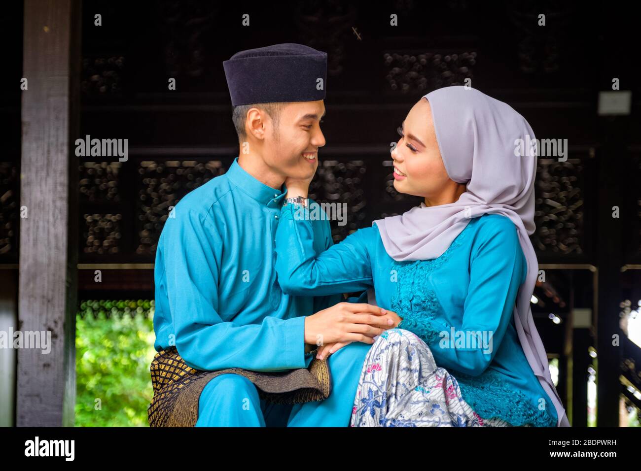 A portrait of young couple of malay muslim in traditional costume showing romantic gesture during Aidilfitri celebration at the traditional wooden hou Stock Photo
