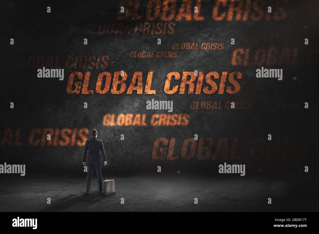 Businessman stands before grunge black wall with 'global crisis' inscription. Conception of recession in business. Stock Photo