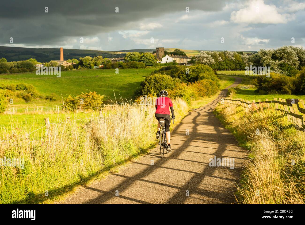 Woman cycling on car free path below Church, Lancashire, part of the Hyndburn Greenway Stock Photo