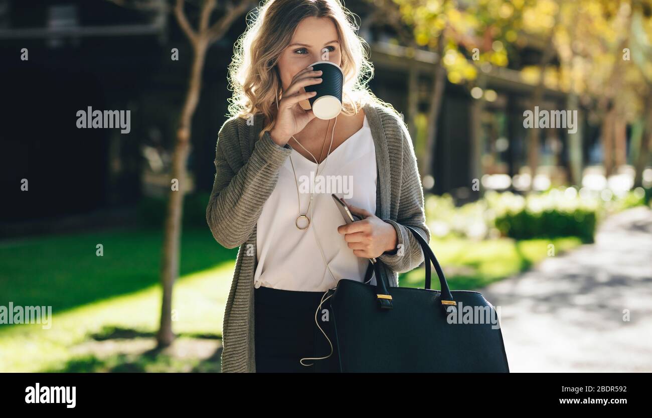 businesswoman with her purse walking on the street and drinking coffee. Woman having coffee while commuting in the city. Stock Photo