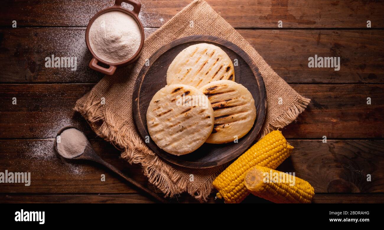 https://c8.alamy.com/comp/2BDRAHG/venezuelan-typical-arepas-made-with-corn-flour-top-view-of-three-arepas-on-a-wooden-plate-and-next-to-it-a-spoon-and-bowl-full-of-cornmeal-on-a-woode-2BDRAHG.jpg