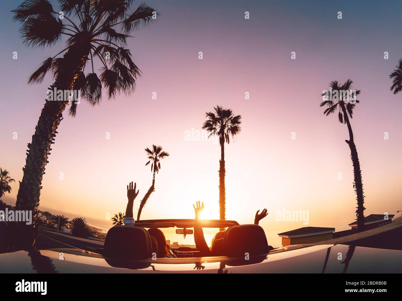 Happy couple having fun during road trip in convertible car - Young lovers enjoying vacation in tropical city Stock Photo