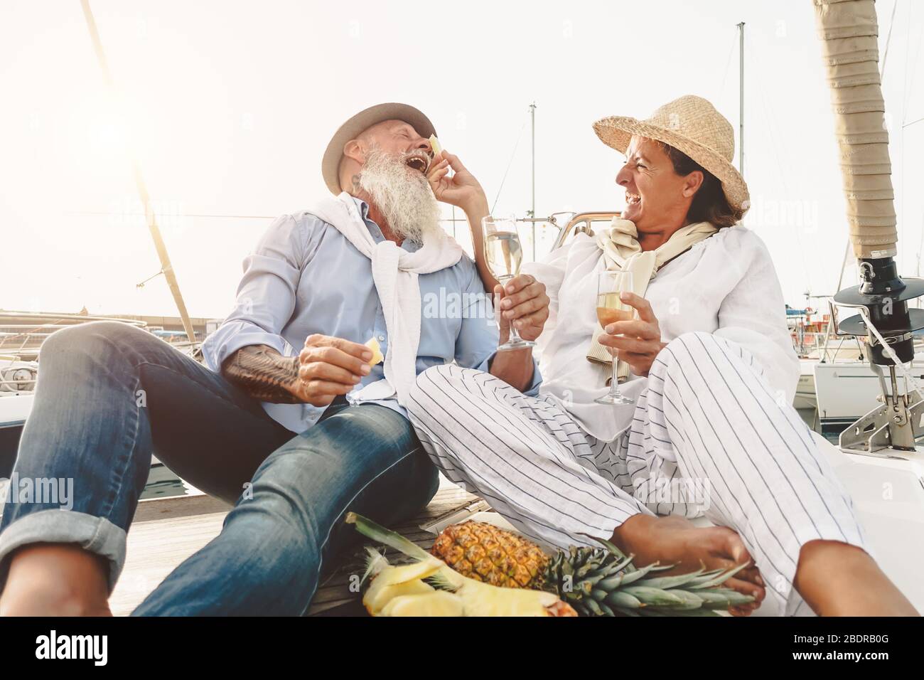 Senior couple drinking champagne eating pineapple on sailboat vacation - Happy mature people having fun celebrating wedding anniversary on boat trip Stock Photo