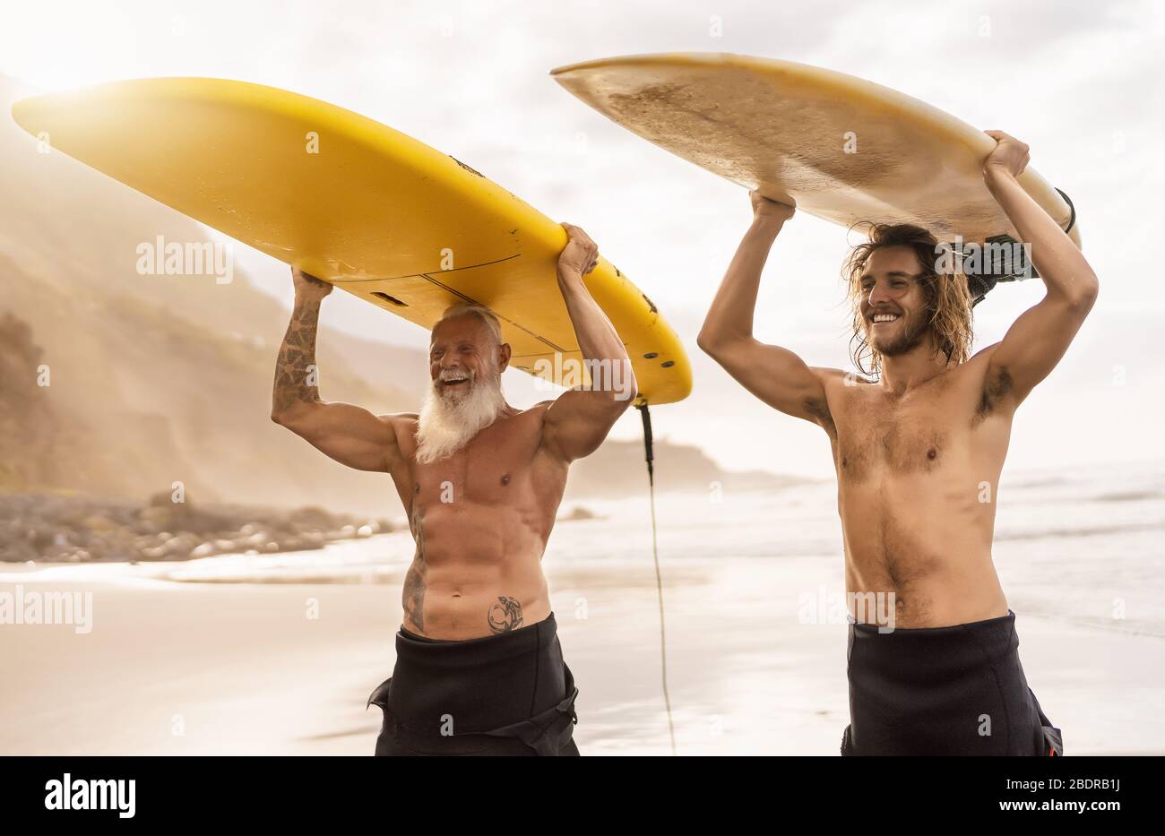 Happy friends surfing together on tropical ocean - Sporty people having fun during vacation surf day - Extreme sport lifestyle concept Stock Photo