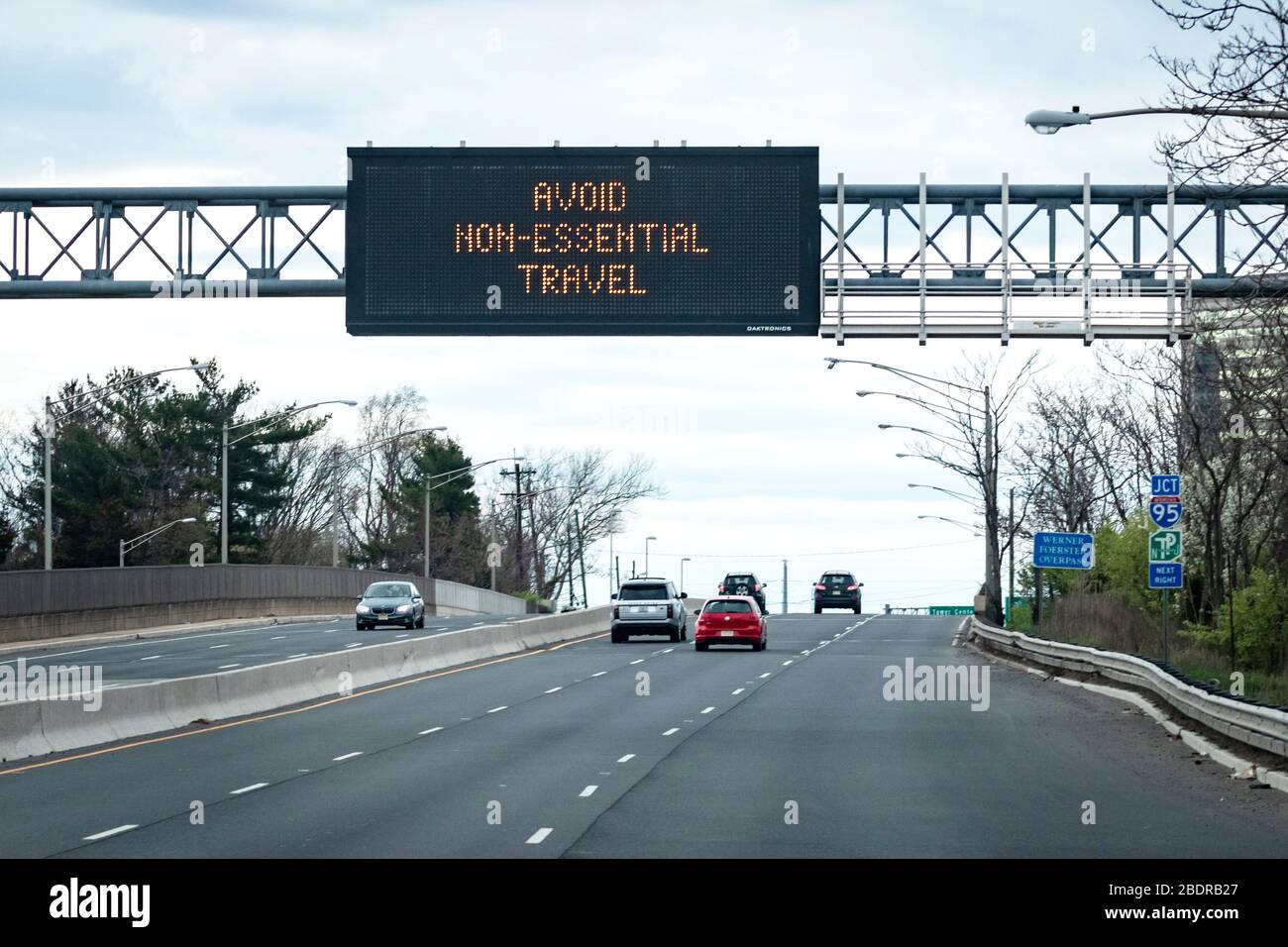 'AVOID NON-ESSENTIAL TRAVEL' message on an electronic traffic message sign, above highway and cars during COVID-19 pandemic Stock Photo