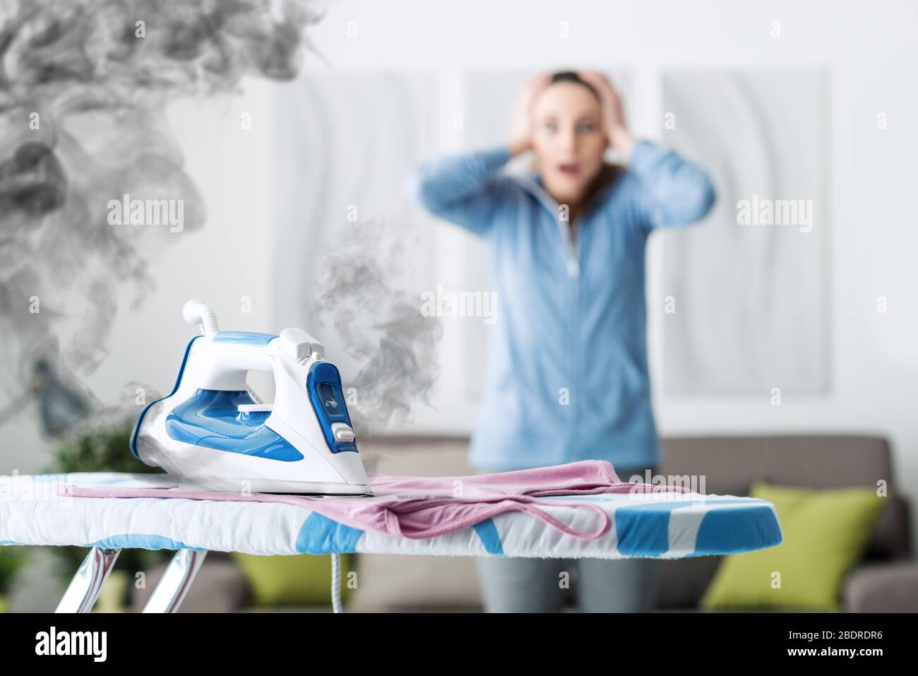 Shocked woman gasping at home, she has left the iron on and she is burning her clothes Stock Photo