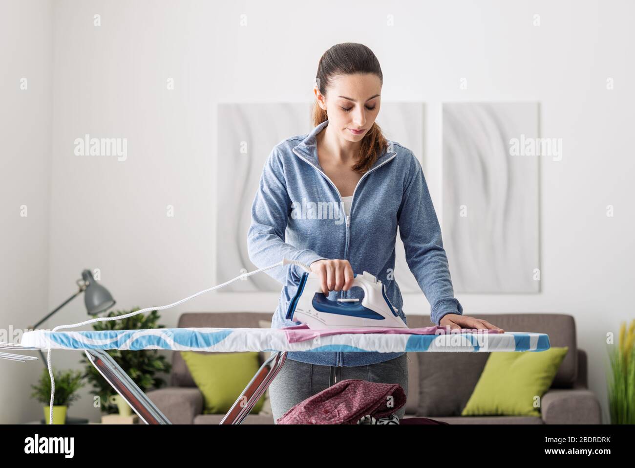 Confident young woman at home ironing her clothes on the ironing board